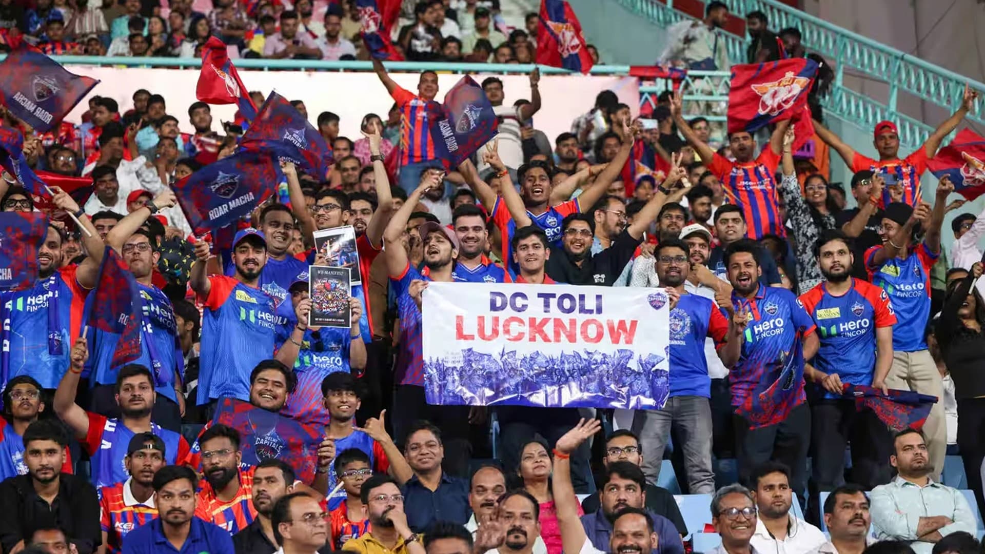Delhi Capitals fans in the stands wearing team jerseys and waving flags