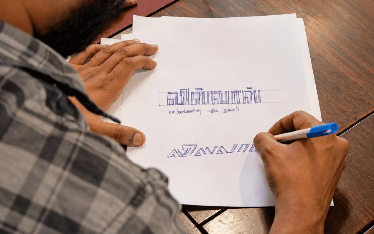 Sketching the Visvas wordmark in Tamil and English on paper